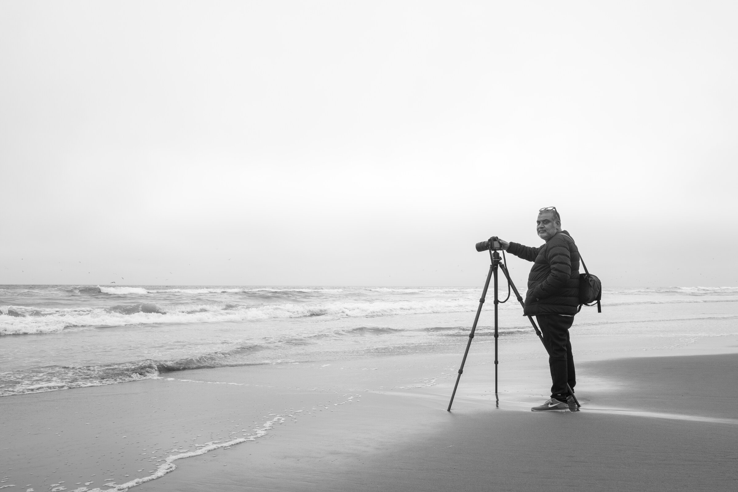 Om Malik at the ocean’s edge at Fort Funston, his camera mounted on a tripod, on a soft grey morning